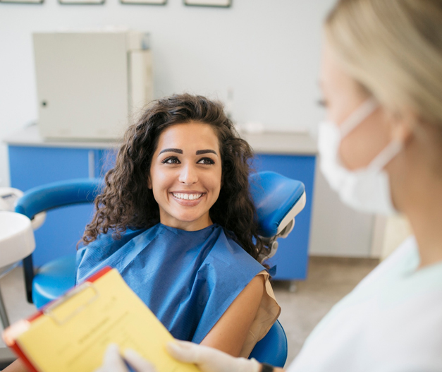 Patient smiling in dental chair while dentist consults with clipboard in modern clinic.