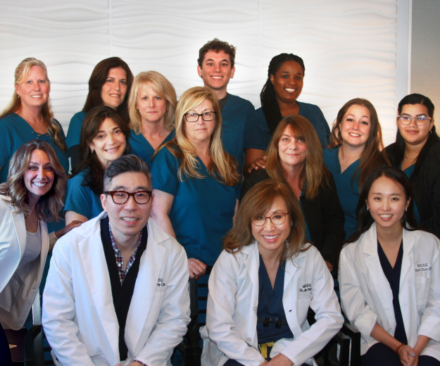 Medical team posing together for group photo in clinical setting, wearing scrubs and lab coats.