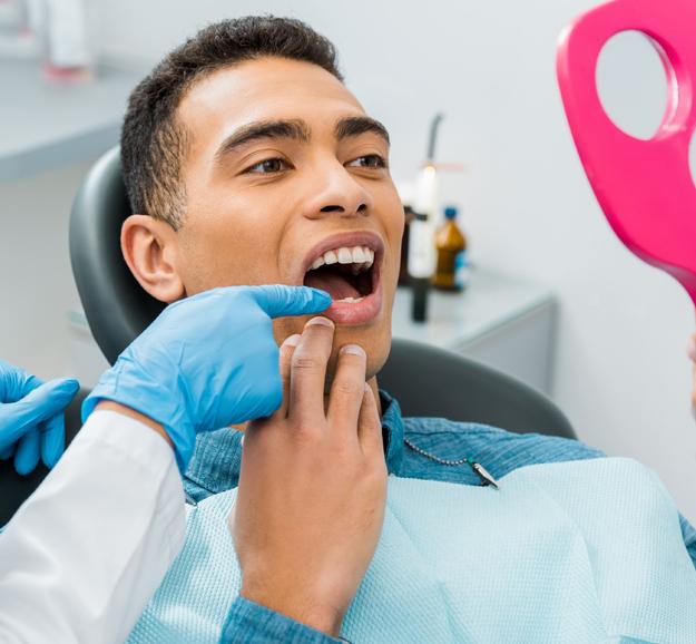 Dentist in blue gloves examining patient's teeth in dental office clinic.