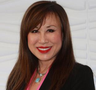 Professional woman with long brown hair and red lipstick smiling at camera, wearing black blazer and pink top.