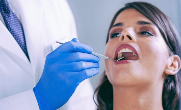 Dentist in blue gloves examining patient's teeth during dental checkup appointment.