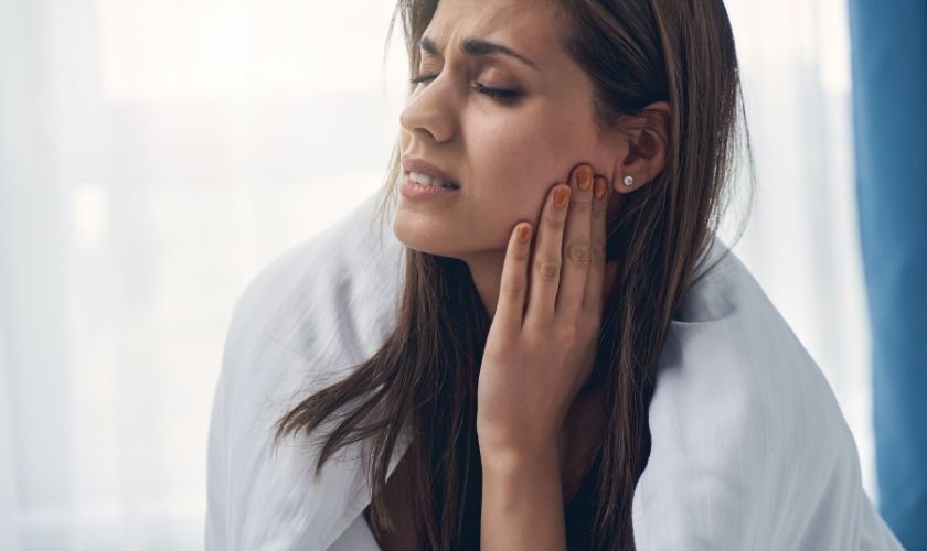 Woman holding her cheek in pain, illustrating tooth discomfort when biting down.